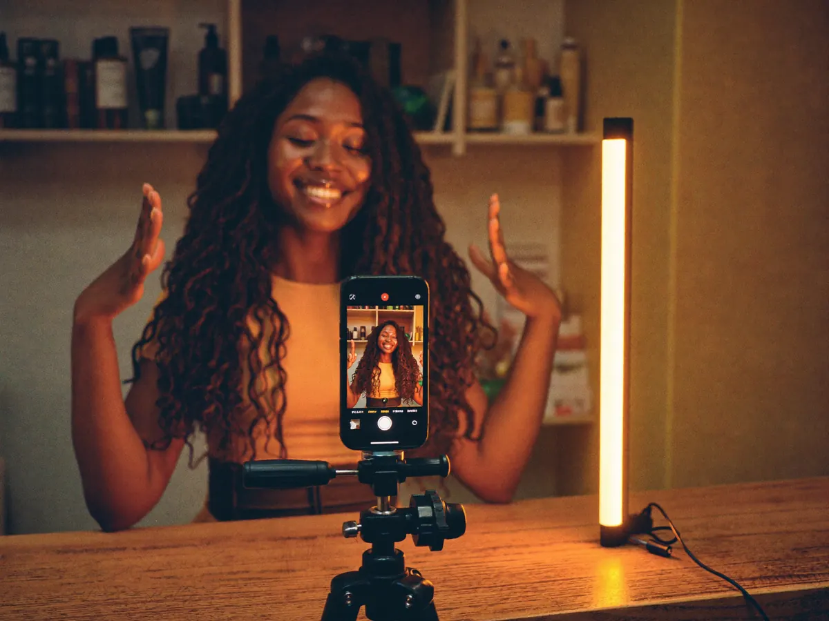 Dona de salão gravando um vídeo com o celular no tripé e um bastão de LED